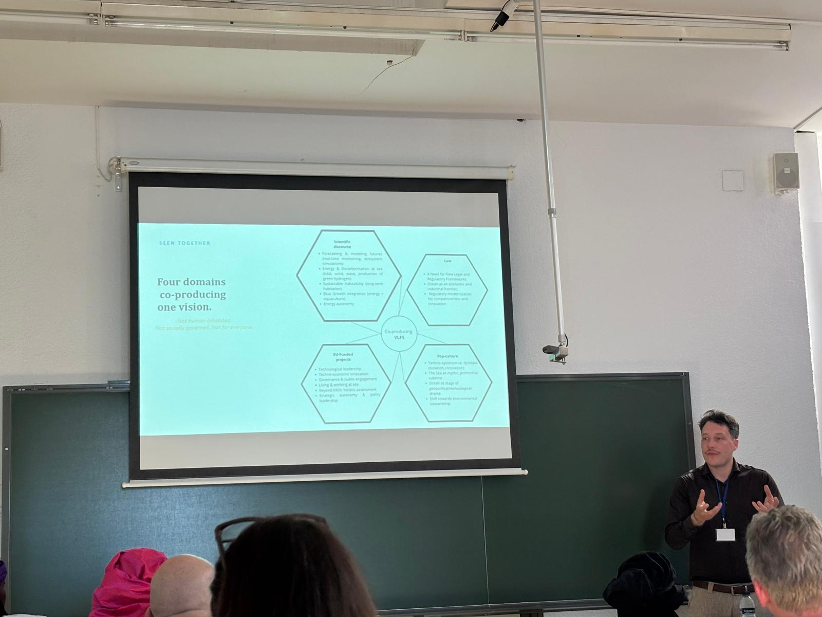A presenter discussing a slide on four domains co-producing a vision for floating structures at sea